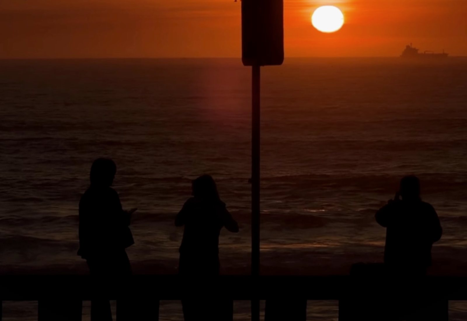 Três pessoas em silhueta contra o pôr do sol no mar