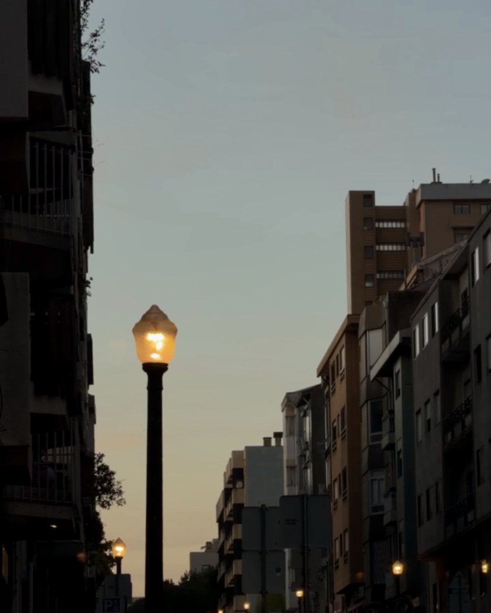 Um candeeiro a acender ao anoitecer numa rua residencial